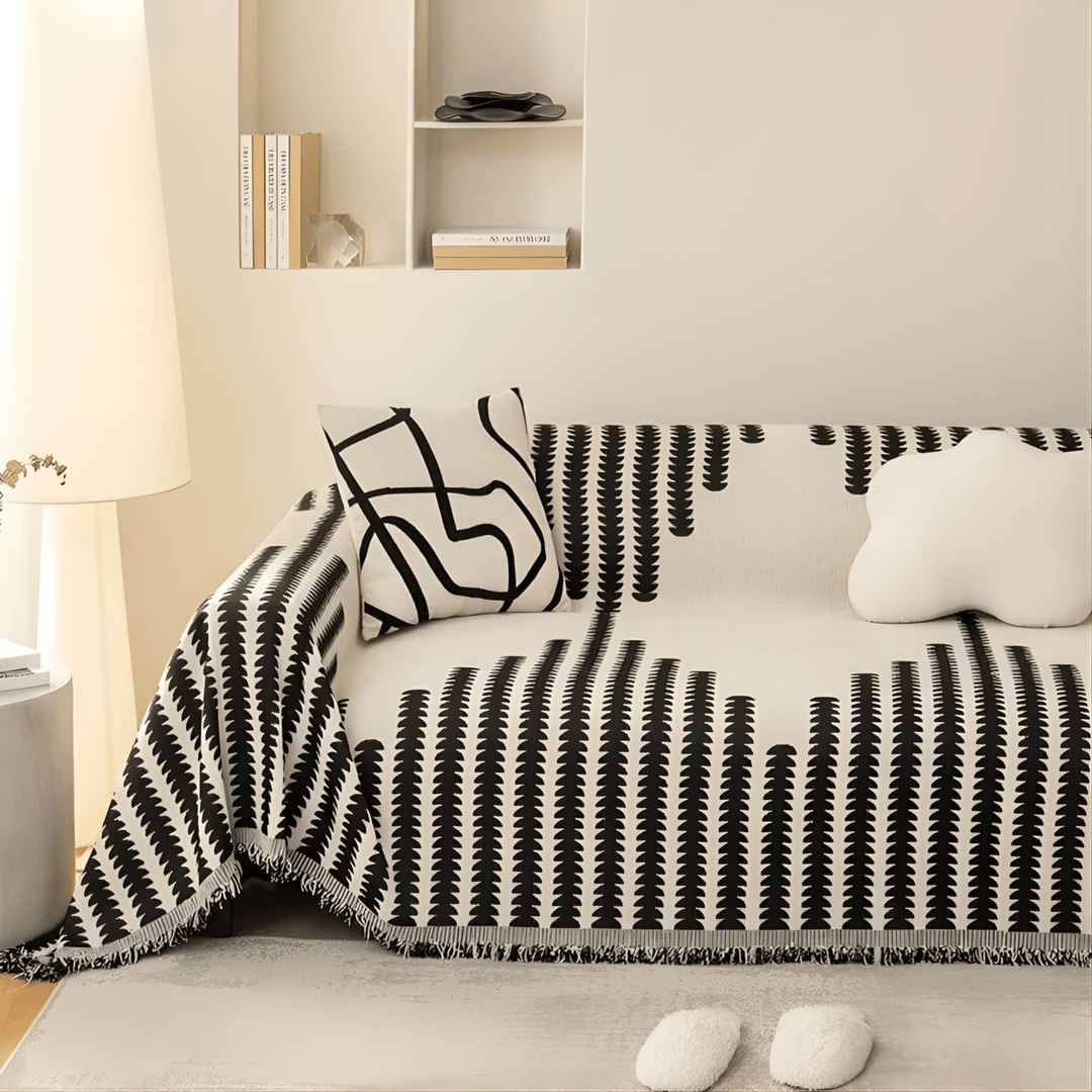 Sofabezug in Schwarz-Weiß mit Fransen an einem Sofa in warm beleuchtetem Raum, mit gemustertem Kissen und Wolkenkissen. 3