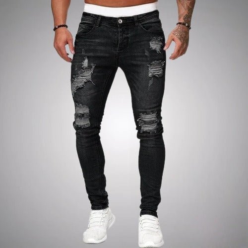 Frontansicht der schmal geschnittenen Distressed-Jeans in Schwarz, getragen mit weißen Sneakern, mit Rissen an Oberschenkeln und Knien. 1