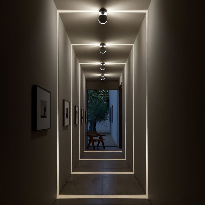 Abendliche Flurszene mit abgedunkeltem Raum, in dem die Leuchten leuchtende quadratische Lichtlinien an Wände und Boden projizieren. 8