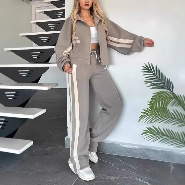 Graues Set mit hellen Streifen, Model lehnt seitlich an der Wand neben einer Treppe, weite Hose mit Kordelzug. 6