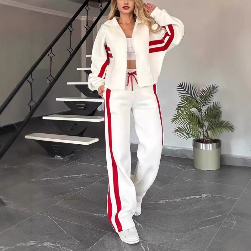 Model in weißem Set mit roten Kontraststreifen, offene Jacke über weißem Top, Hose mit weitem Bein, vor einer Treppe stehend. 1