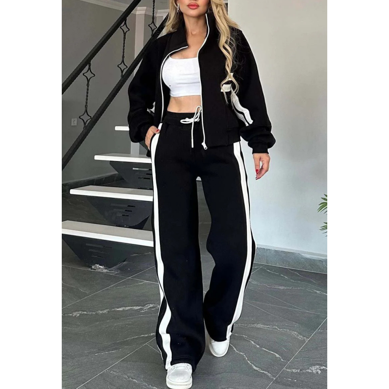 Schwarzes Set mit weißen Streifen, Jacke offen über weißem Top, Hand in der Hosentasche, weiße Kordel am Bund sichtbar. 4