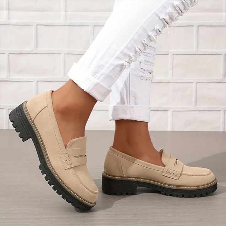 Beigefarbene Loafer mit dicker schwarzer Profilsohle, getragen zu weißer Jeans mit Rissen vor weißer Backsteinwand. 3