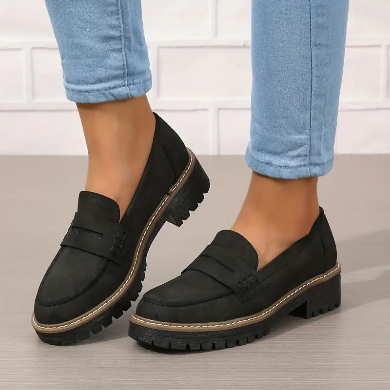 Schwarze Loafer mit Zierlasche und kräftiger Profilsohle, getragen zu blauer Jeans vor heller Backsteinwand. 6