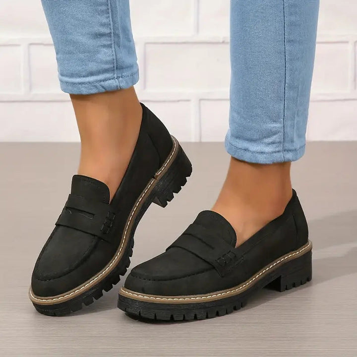 Schwarze Loafer mit Zierlasche und kräftiger Profilsohle, getragen zu blauer Jeans vor heller Backsteinwand. 6