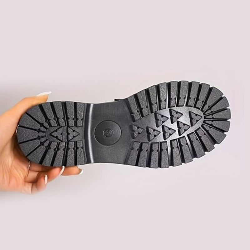 Schwarze Profilsohle von unten, von einer Hand gehalten, mit grobem Stollenmuster und rundem Logo in der Mitte. 10