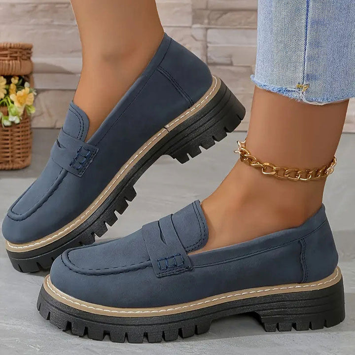 Blaue Wildleder-Loafer mit Plateausohle, getragen mit goldener Fußkette zu Jeans vor Steinwand. 16