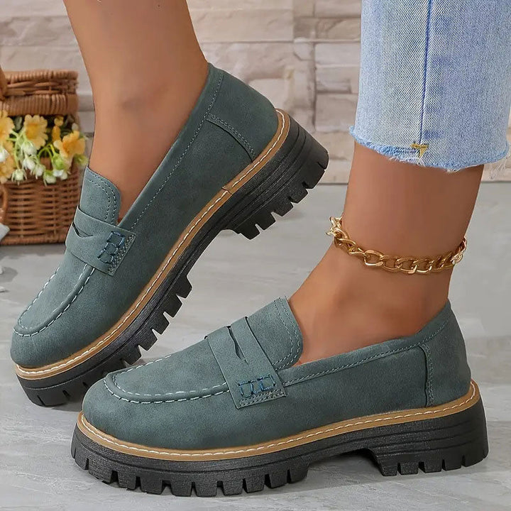 Graugrüne Wildleder-Loafer mit blauen Ziernähten an der Lasche und Plateausohle, getragen mit goldener Fußkette. 15