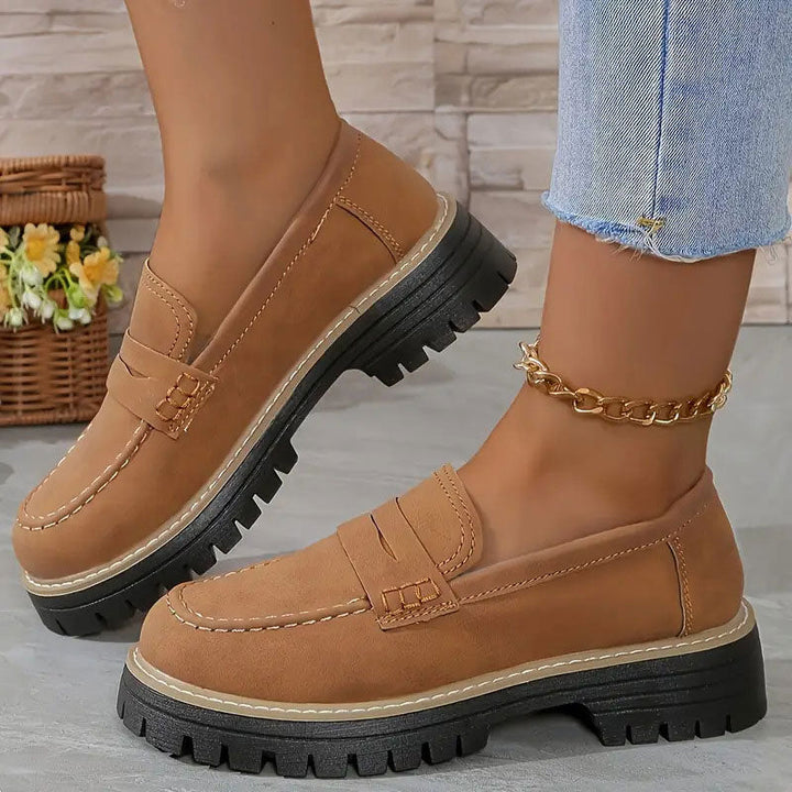Hellbraune Loafer mit orangefarbener Ziernaht und schwarzer Plateausohle, getragen mit goldener Fußkette. 17