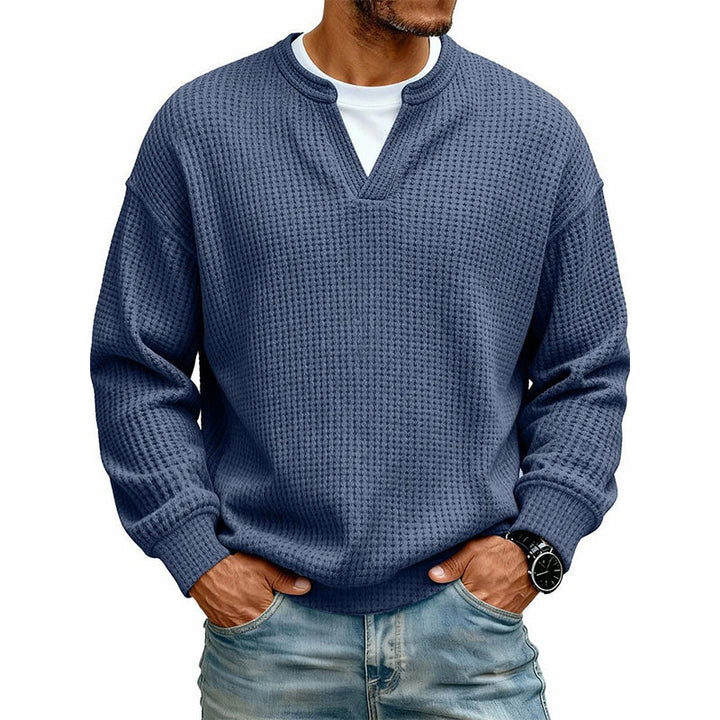Frontansicht des Oberteils in dunklem Blau am Model, mit weißem Shirt unter dem V-Ausschnitt, Hände in den Jeanstaschen. 13