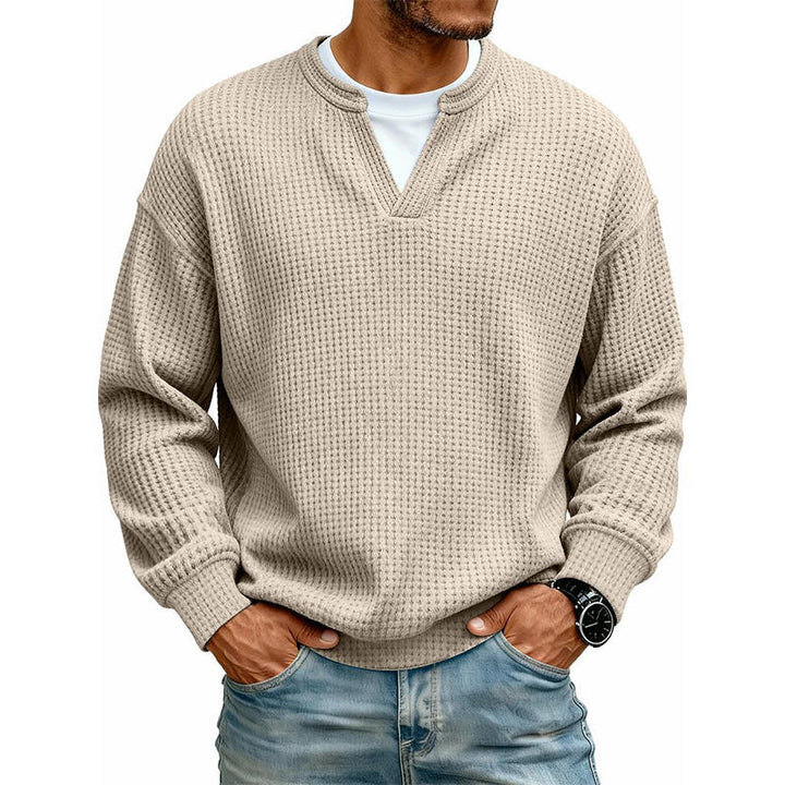 Frontansicht des Oberteils in Beige am Model, mit weißem Shirt unter dem V-Ausschnitt, Hände in den Jeanstaschen. 11