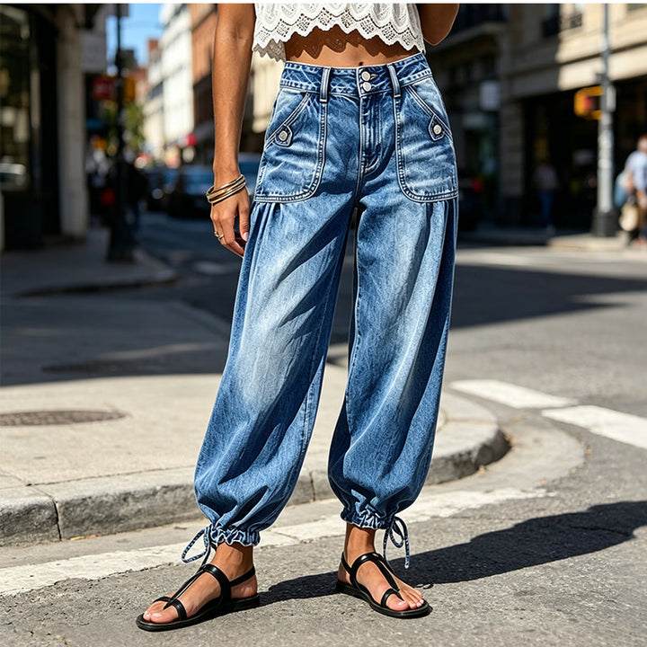 Frontansicht auf der Straße: hellblaue Barrel-Jeans mit hohem Bund, aufgesetzten Taschen und gebundenen Säumen, kombiniert mit Spitzentop und Sandalen. 2