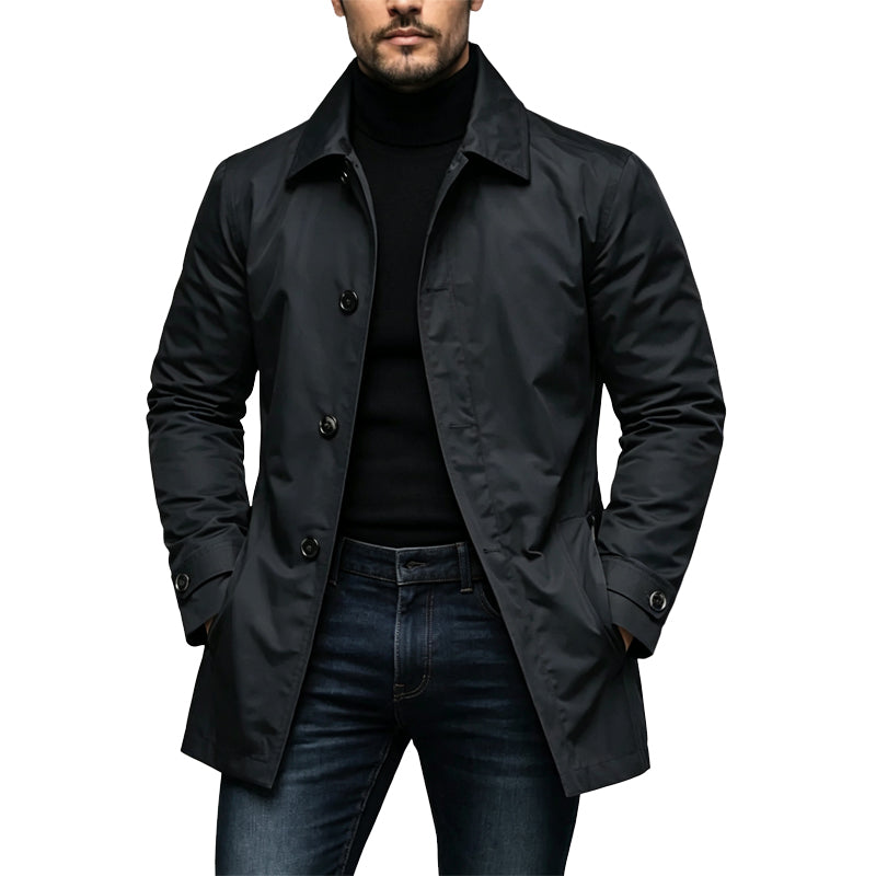 Mann trägt den knielangen Mantel in Schwarz offen über Rollkragenpullover und Jeans, Hände in den Taschen, Frontansicht. 1