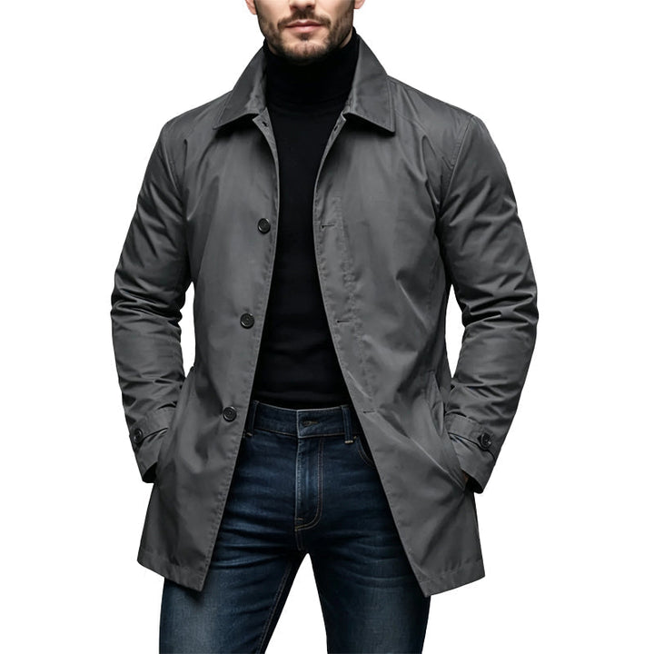 Mantel in Grau an einem Model, vorne dreireihig geknöpft, mit Kragen und Manschettenriegeln, kombiniert mit schwarzem Rollkragen und Jeans. 2