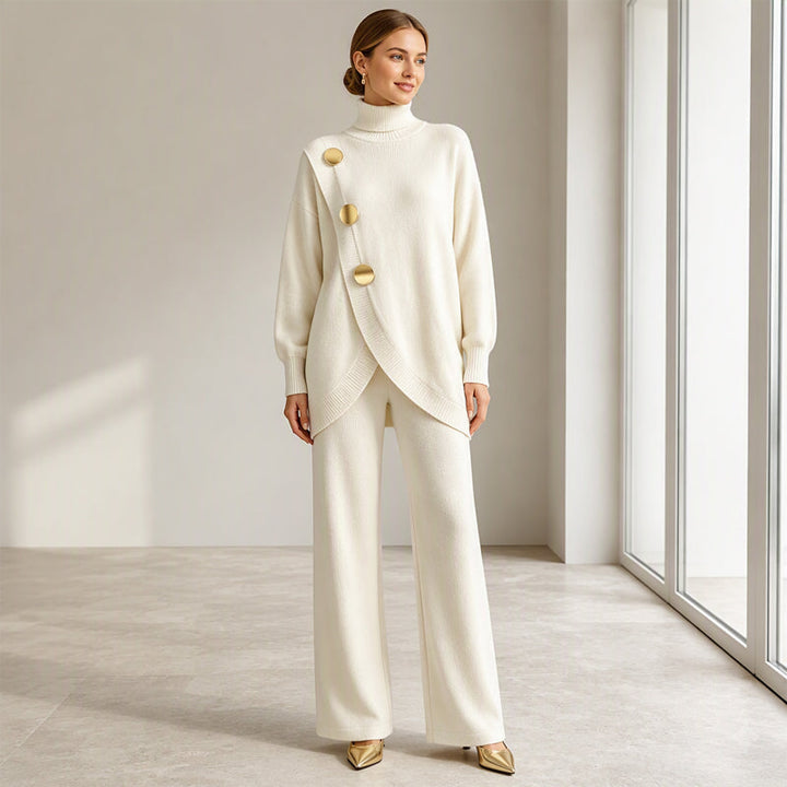 Lächelndes Model in cremeweißem Strickset, Arme locker herabhängend, goldene Pumps, frontale Ganzkörperansicht im hellen Raum. 7