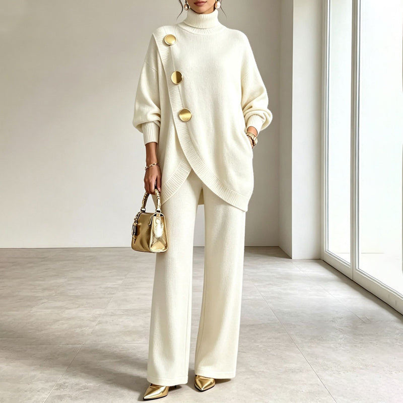 Das Strickset in Cremeweiß, getragen mit goldener Handtasche und goldenen Pumps, Hand in der Hosentasche, im hellen Raum. 2