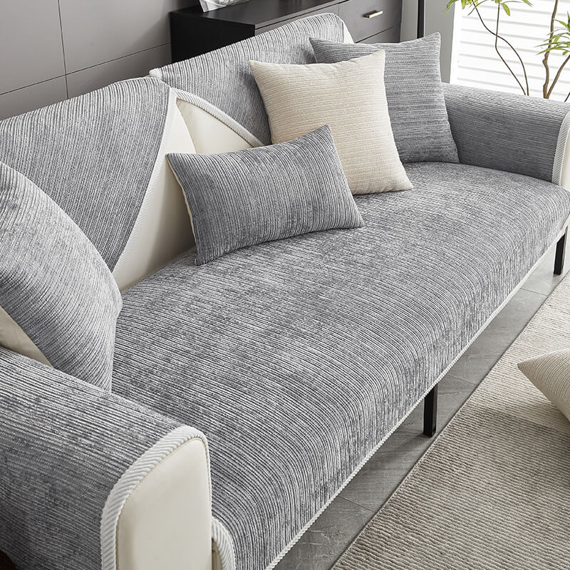 Grauer gestreifter Chenille-Sofabezug mit heller Zierkante auf einem Sofa, dekoriert mit grauen und cremefarbenen Kissen, Blick von schräg oben. 1