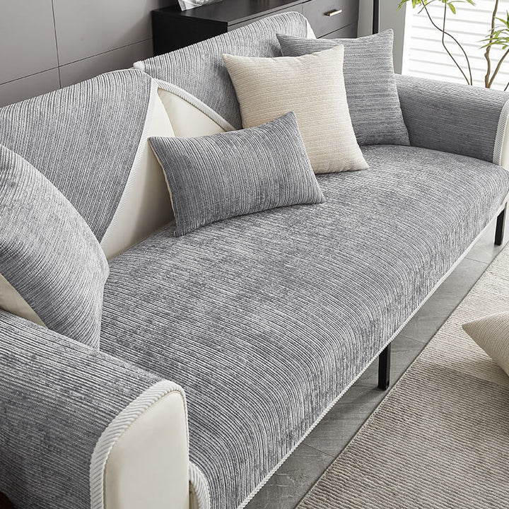 Grauer gestreifter Chenille-Sofabezug mit heller Zierkante auf einem Sofa, dekoriert mit grauen und cremefarbenen Kissen, Blick von schräg oben. 1