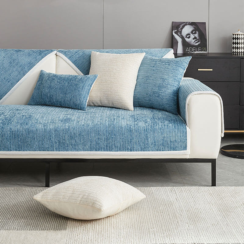 Blauer Chenille-Sofabezug auf einem weißen Sofa vor dunkler Kommode, dazu blaue und cremefarbene Kissen sowie ein Kissen auf dem Boden. 11