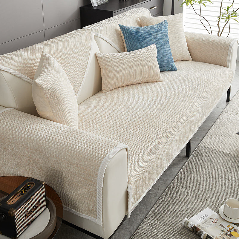 Cremefarbener Chenille-Sofabezug auf einem hellen Sofa, mit cremefarbenen Kissen und einem blauen Akzentkissen, daneben Beistelltisch. 3