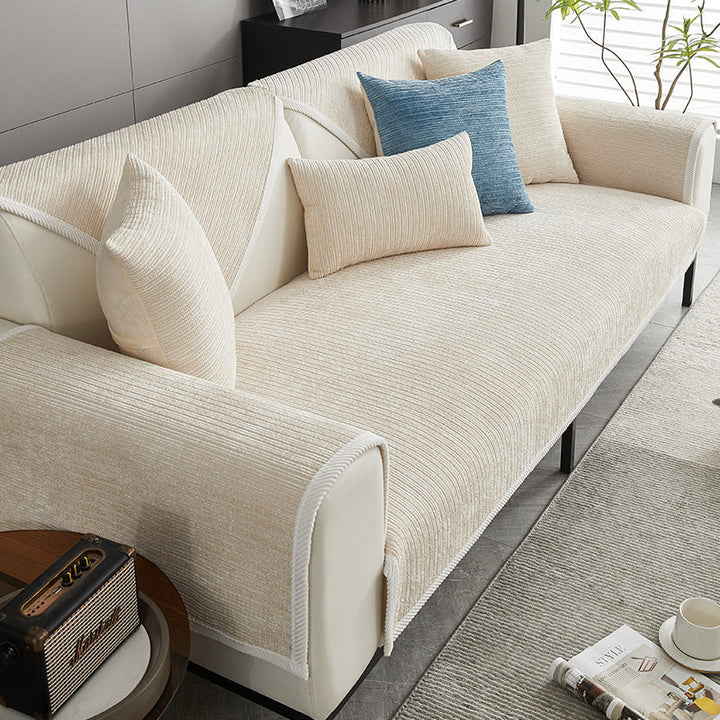 Cremefarbener Chenille-Sofabezug auf einem hellen Sofa, mit cremefarbenen Kissen und einem blauen Akzentkissen, daneben Beistelltisch. 3
