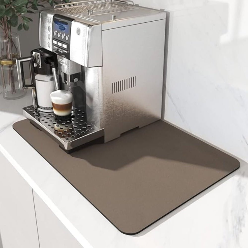 Braune Unterlage unter einem Kaffeevollautomaten, der gerade einen Milchkaffee im Glas zubereitet, auf weißer Arbeitsplatte. 3
