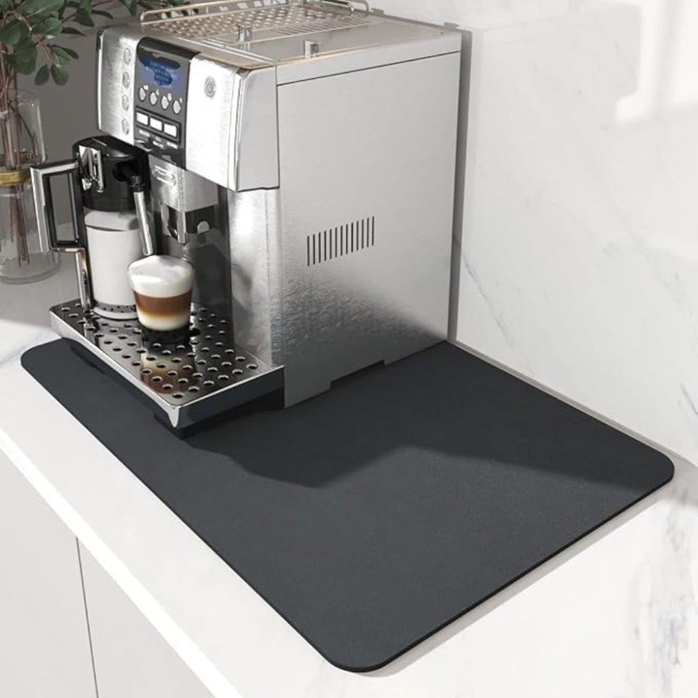 Dunkelgraue Unterlage unter einem Kaffeevollautomaten mit Milchbehälter und einem Latte macchiato auf heller Marmor-Arbeitsplatte. 2