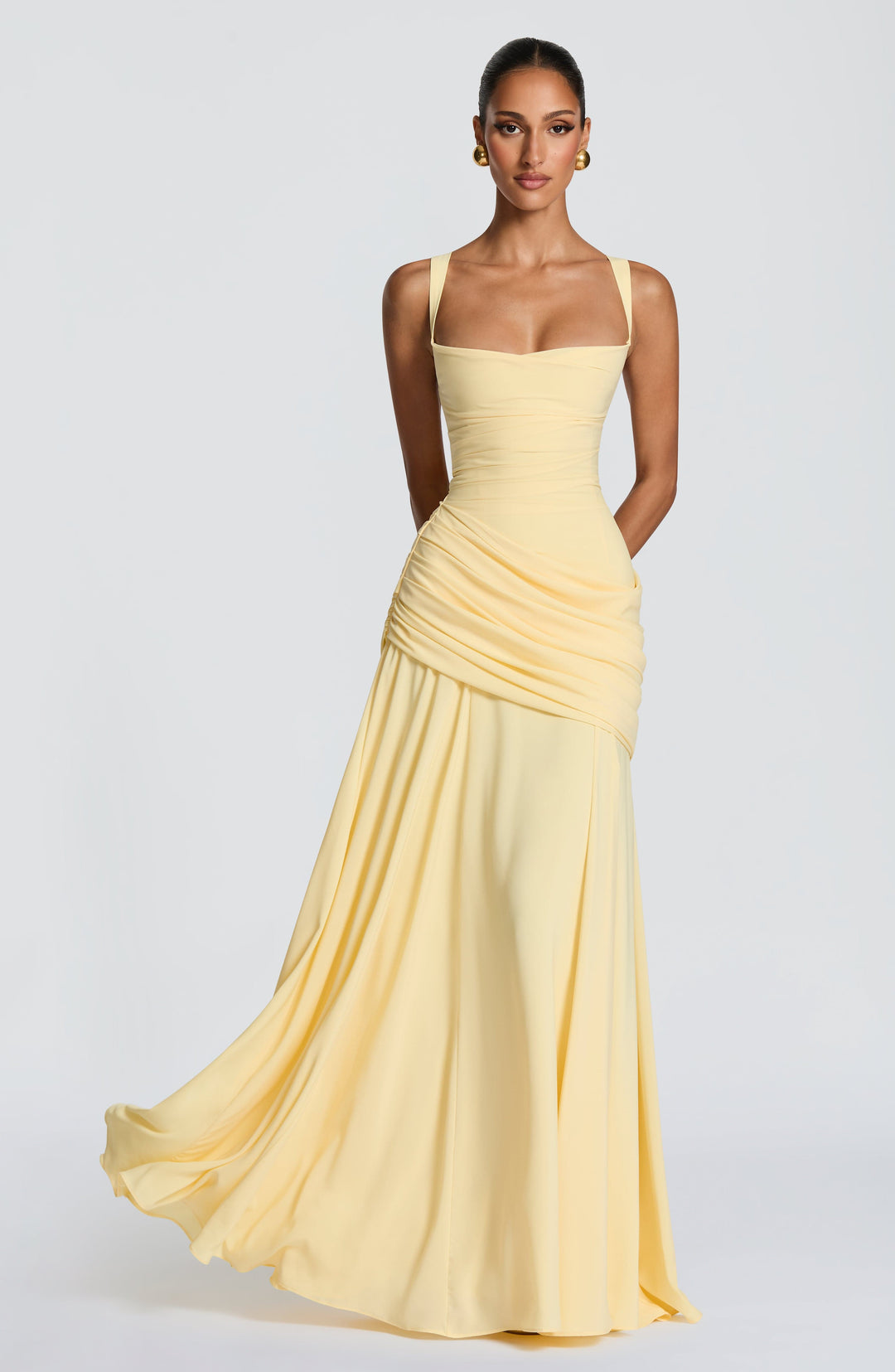 Model in hellgelbem Maxikleid mit eckigem Ausschnitt, drapiertem Hüftteil und weit schwingendem Rock, frontal vor hellem Hintergrund. 1