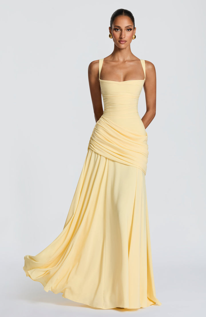 Model in hellgelbem Maxikleid mit eckigem Ausschnitt, drapiertem Hüftteil und weit schwingendem Rock, frontal vor hellem Hintergrund. 1