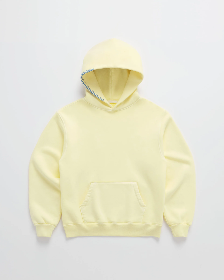 Hellgelber Kapuzenpullover von vorn auf hellem Grund, mit Känguru-Tasche und blauer Ziernaht am Kapuzenrand. 1