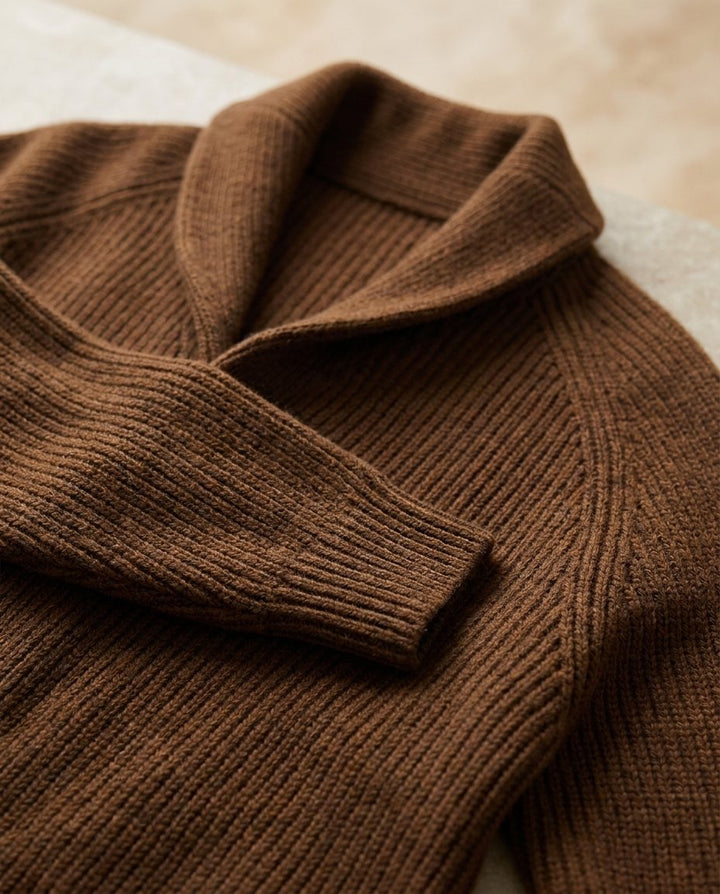 Nahaufnahme der braunen Strickjacke mit Schalkragen, Raglanärmel und Rippbündchen, die die Strickstruktur im Detail zeigt. 13