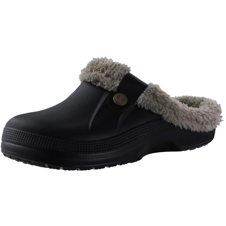 Schwarzer Clog mit grauem Plüschfutter, Zierknopf am Riemen und profilierter Sohle, schräg von vorne auf weißem Hintergrund fotografiert. 1