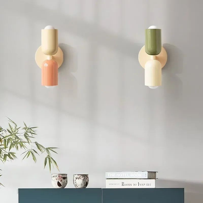 Zwei Wandlampen nebeneinander, links Creme mit Lachs, rechts Grün mit Creme, über einem Sideboard mit Büchern und Pflanze. 14