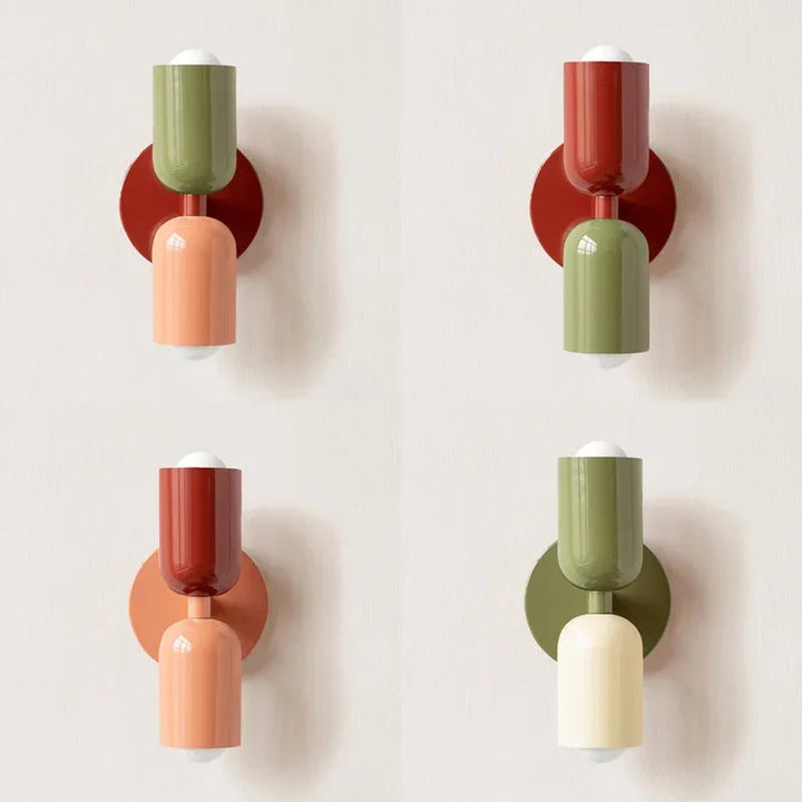 Vier Farbvarianten der Wandlampe nebeneinander an heller Wand, kombiniert aus Grün, Lachs, Rot und Creme. 12