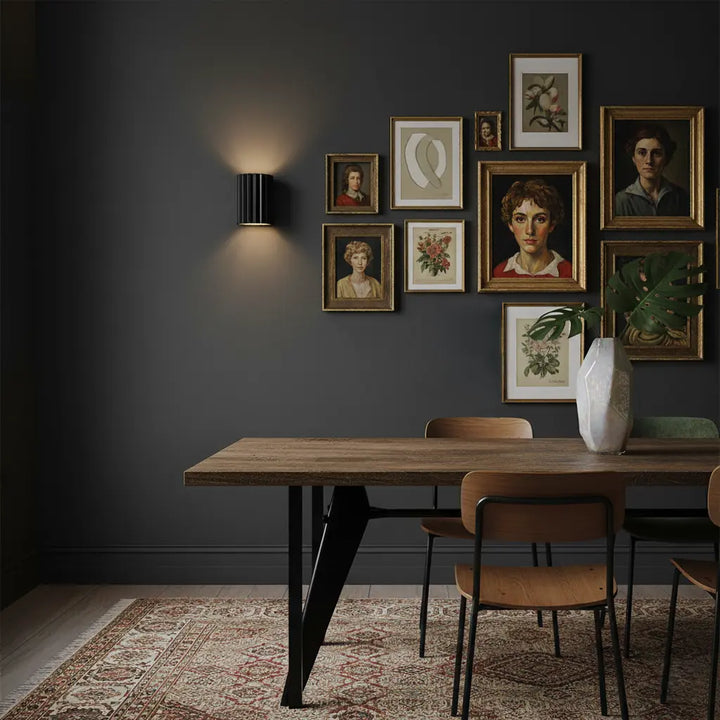 Schwarze gerippte Wandlampe an dunkler Wand neben einer Bildergalerie über einem Holzesstisch 6