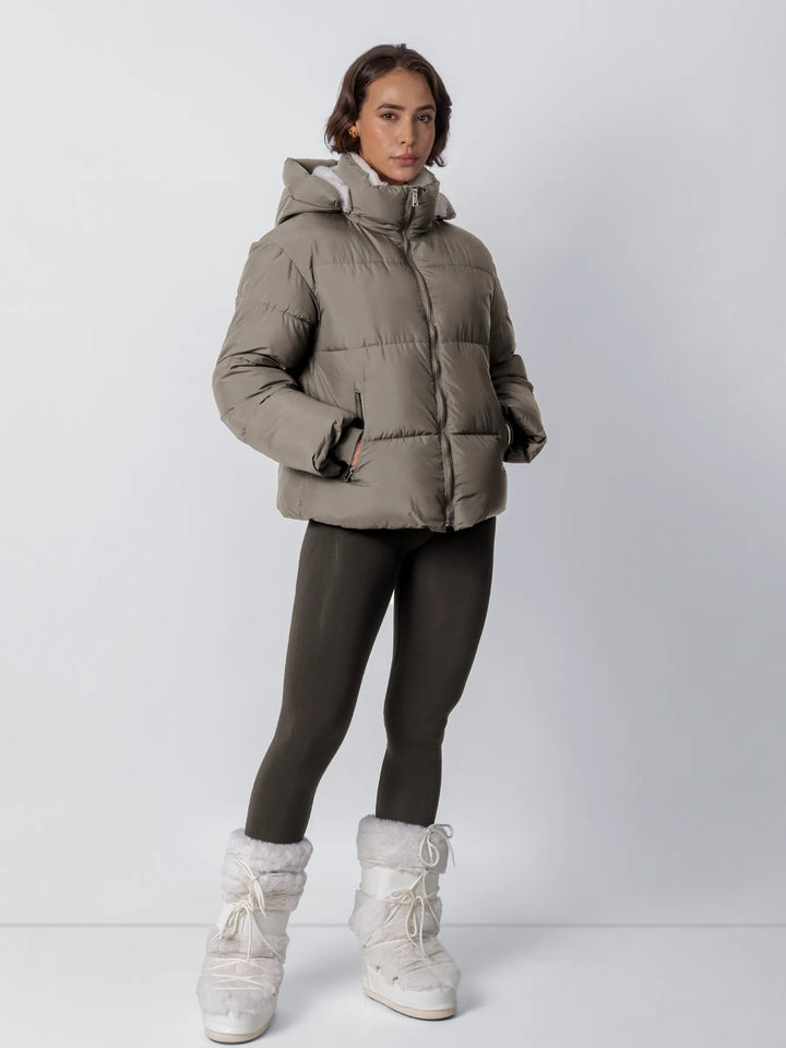 Model in graubrauner Steppjacke mit Fleecefutter, dunklen Leggings und weißen Fellstiefeln, Ganzkörperansicht von vorn, Hände 21