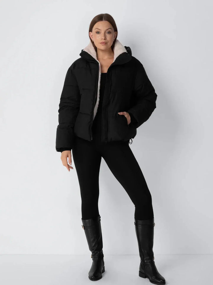 Ganzkörperansicht der schwarzen Steppjacke mit hellem Futter, kombiniert mit schwarzer Leggings und hohen Stiefeln 13