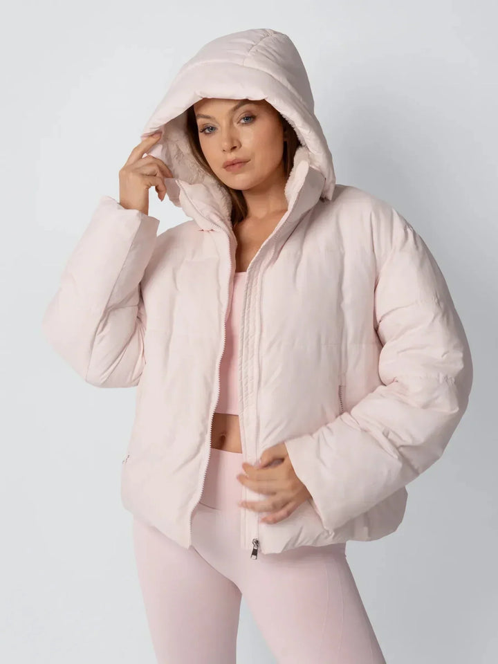 Model in rosafarbener Steppjacke mit hochgezogener Kapuze und Fleecefutter, eine Hand am Kapuzenrand 6