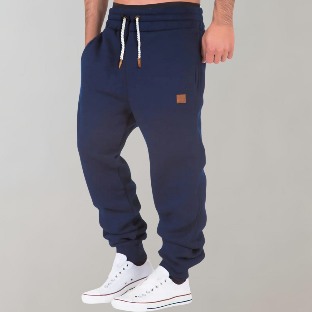 Dunkelblaue Jogginghose mit Kordelzug und eingesteckten Händen, seitlich getragen mit weißen Sneakers 5