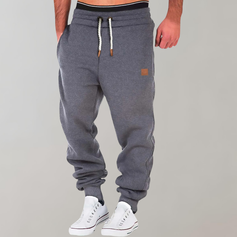Graue Jogginghose mit Kordelzug und Beinbündchen, von einem Model mit weißen Sneakers getragen 2