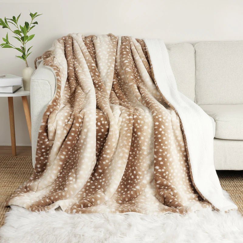 Braun-beige gepunktete Kuscheldecke locker über ein helles Sofa drapiert, die weiße Sherpa-Seite hängt an der Seite herunter. 1