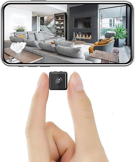 Winzige quadratische Kamera zwischen zwei Fingern gehalten, darüber ein Smartphone mit Live-Bild eines modernen Wohnzimmers. 1