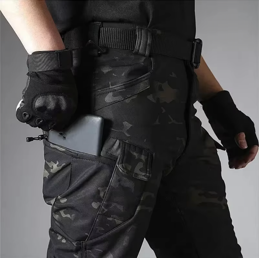Detail der Camouflage-Hose am Model: Smartphone steckt in der Reißverschlusstasche am Oberschenkel, dazu Gürtel und schwarze Handschuhe. 19