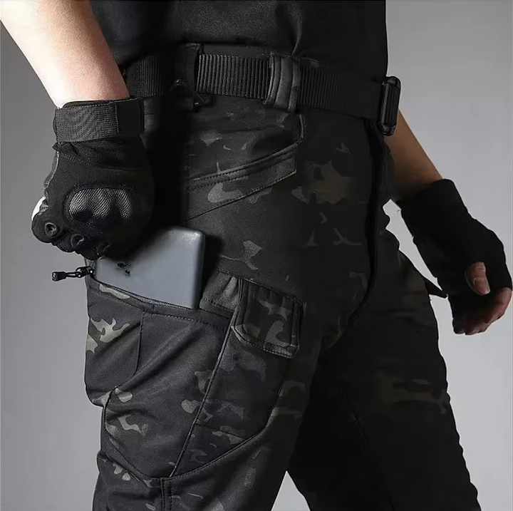 Detail der Camouflage-Hose am Model: Smartphone steckt in der Reißverschlusstasche am Oberschenkel, dazu Gürtel und schwarze Handschuhe. 19