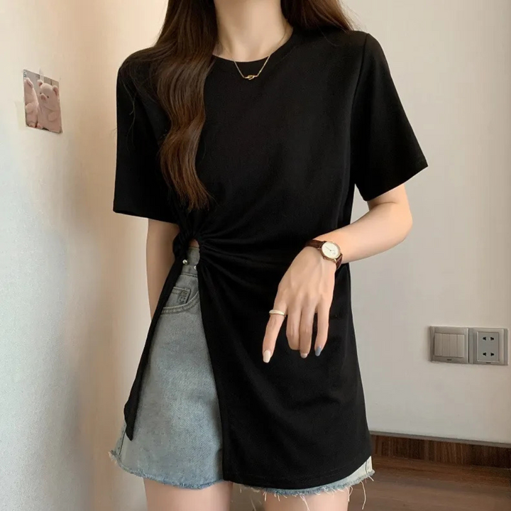 Frau trägt schwarzes T-Shirt mit Knoten, graue Jeansshorts, Armbanduhr, modisch, lässig.